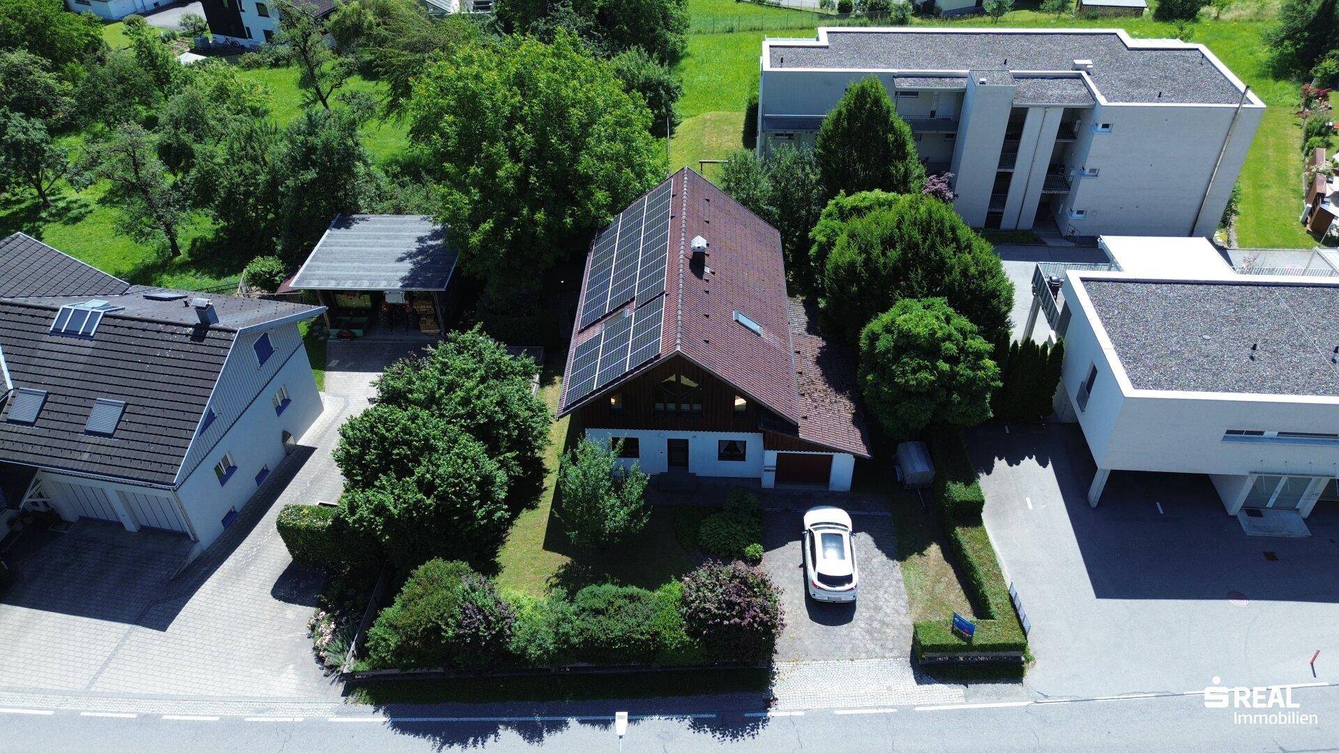 Luftaufnahme des Hauses mit Photovoltaikanlage auf dem Dach und umliegender grüner Landschaft.