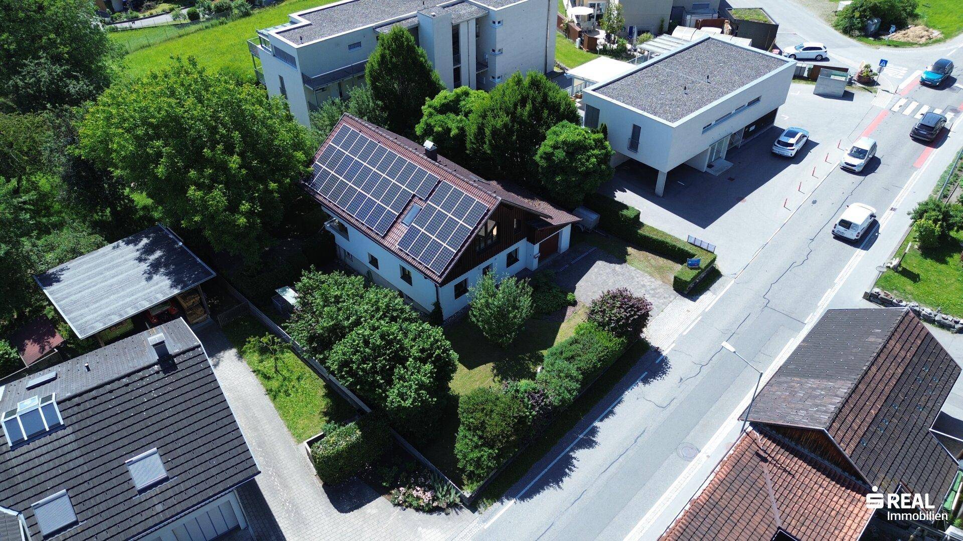 Weitläufige Luftaufnahme des Anwesens mit Photovoltaikanlage, Garten und angrenzender Straße.