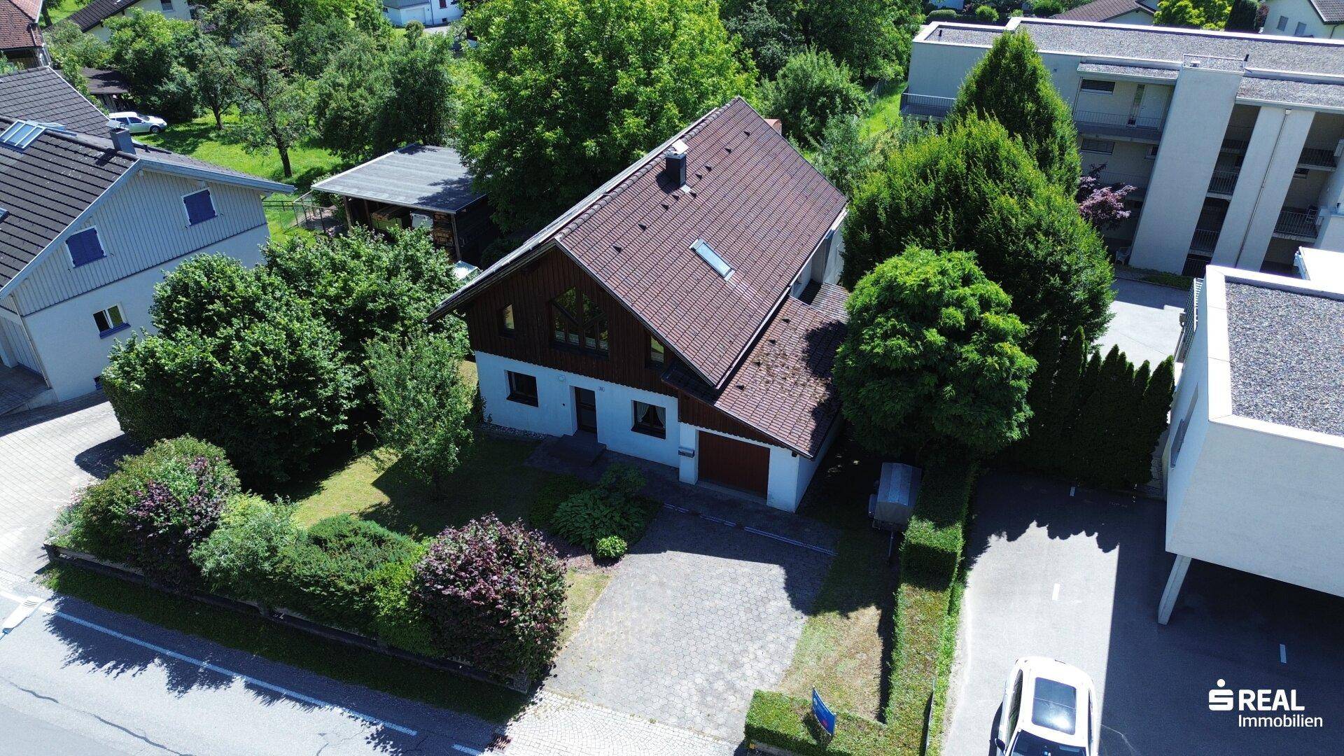 Schrägansicht des Hauses von oben mit Satteldach, gepflegtem Garten und Einfahrt.