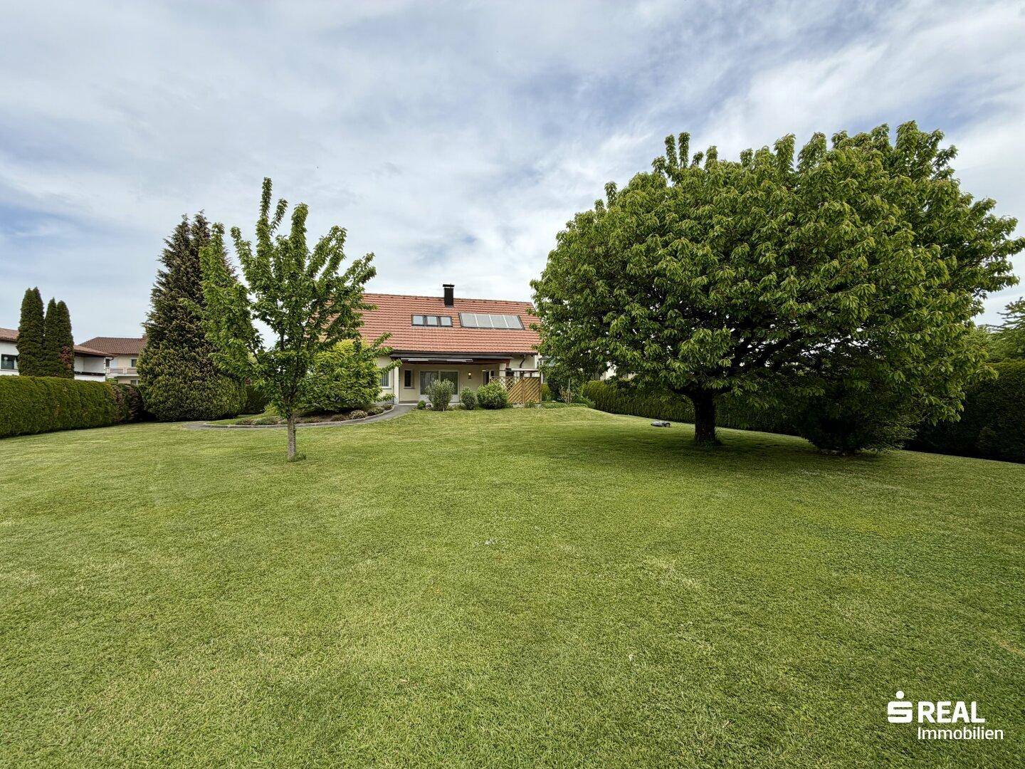 Weitläufiger Garten mit gepflegtem Rasen, Bäumen und Blick auf das Wohnhaus.