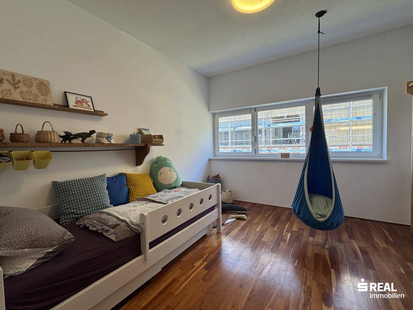 Kinderzimmer mit Holzboden, großem Fenster und Hängesessel.