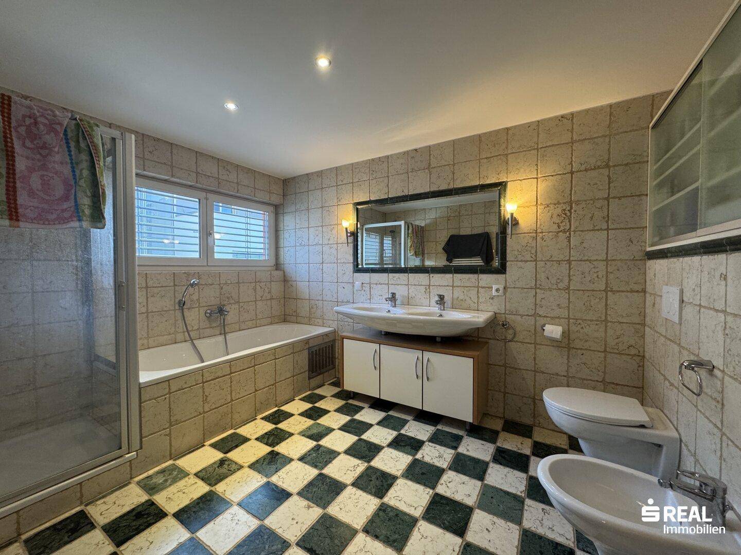 Geräumiges Badezimmer mit Badewanne, Dusche, Doppelwaschbecken und Fenster.