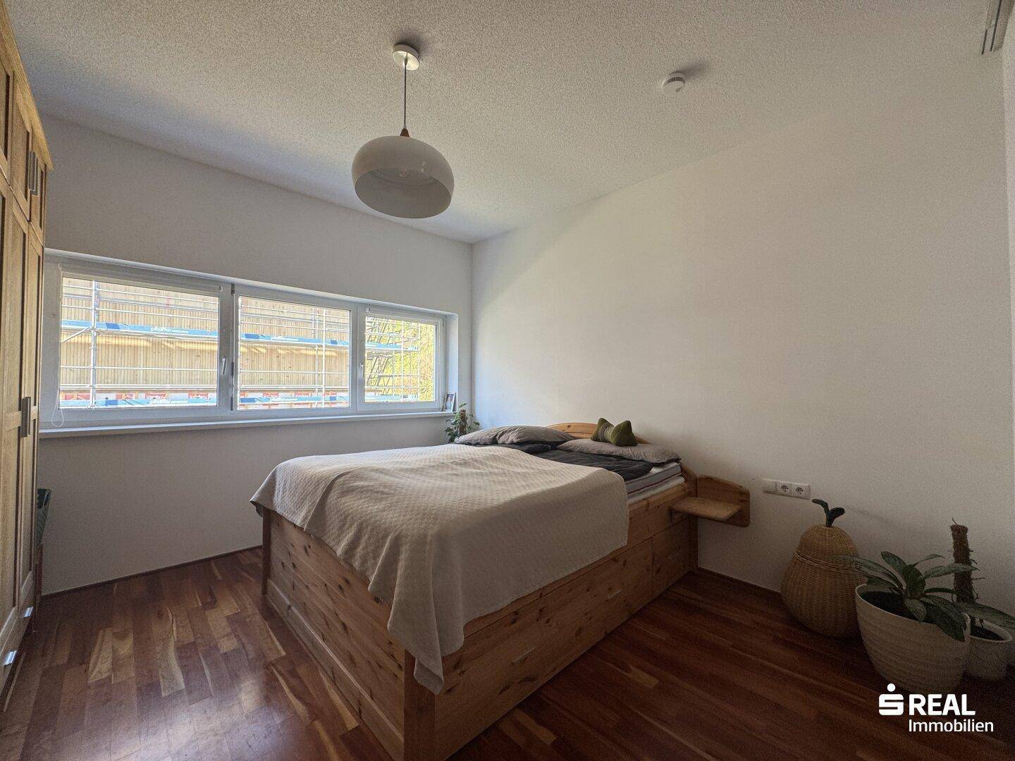 Schlafzimmer mit Holzbett, Holzschrank und großen Fenstern.