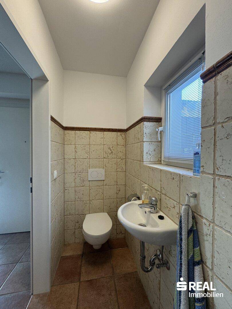 Kleines Gäste-WC mit Fenster, Waschbecken und Wand-WC.
