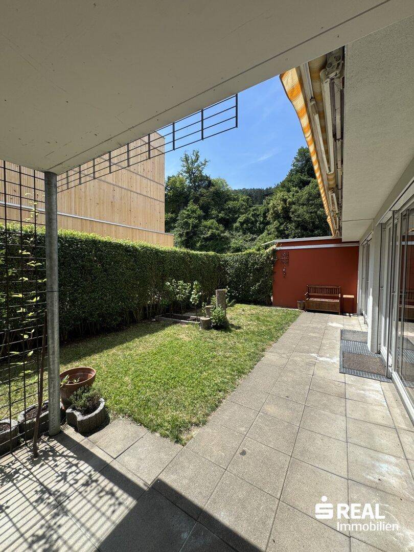 Gepflegter Gartenbereich mit Terrasse, Rasen und Sitzbank.