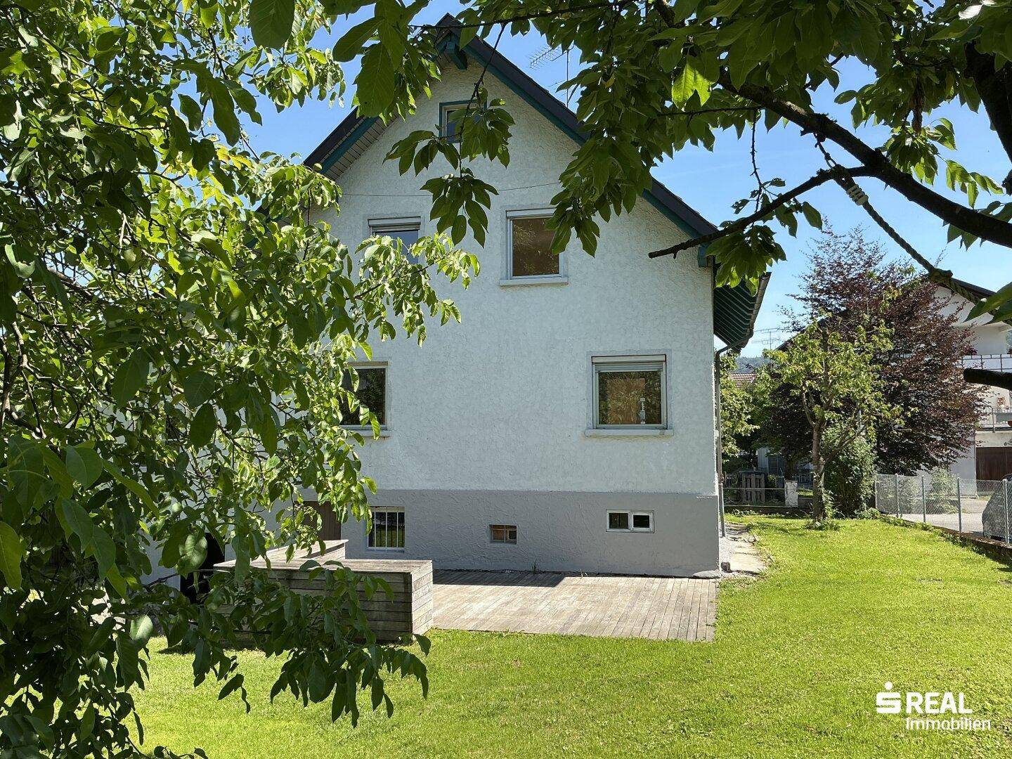 Blick auf die Rückseite des Hauses und den weitläufigen Garten, umgeben von Bäumen.