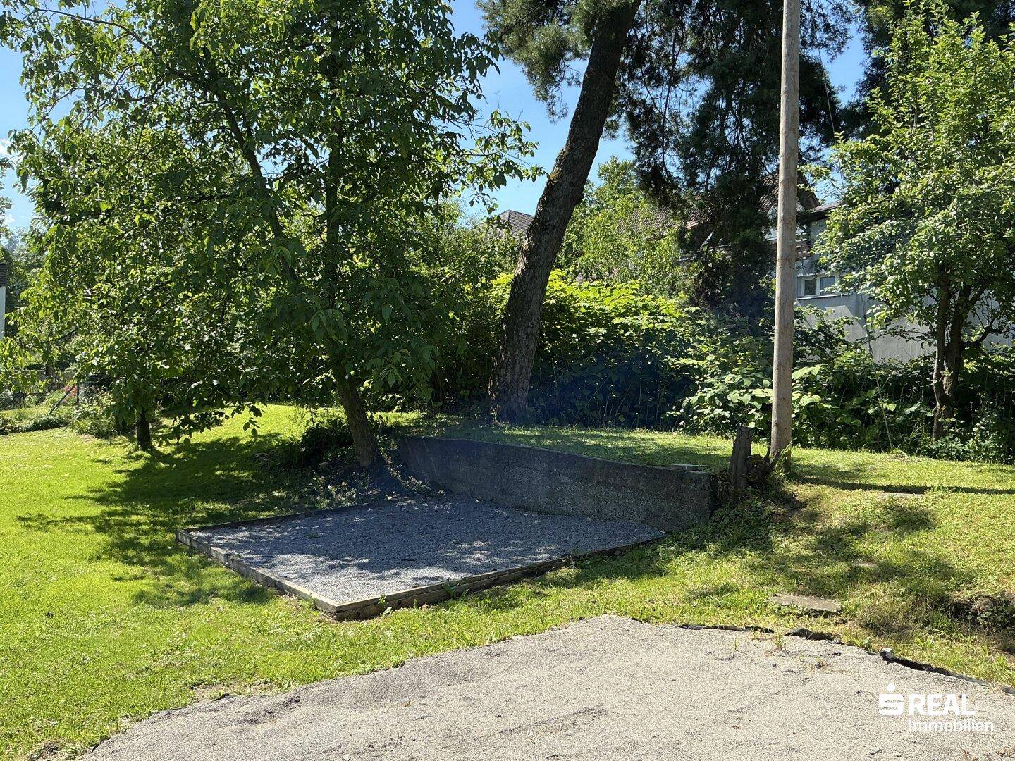 Kiesfläche im Garten, umgeben von Rasen und Bäumen, ideal für eine Sitzecke.
