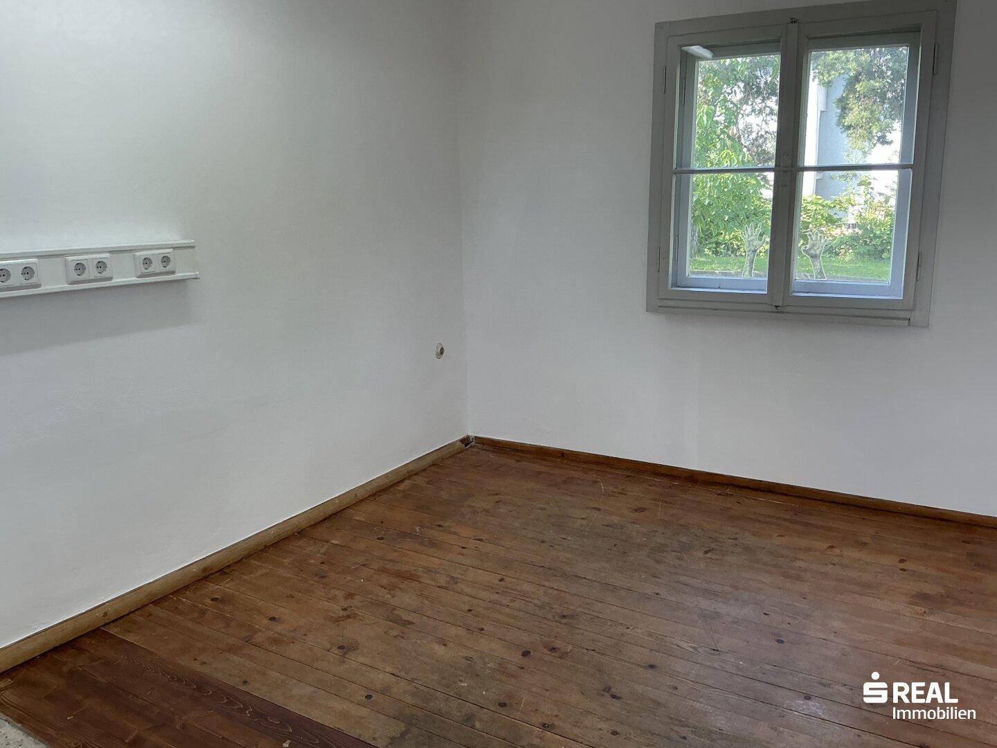 Helles Zimmer mit Holzdielenboden und Blick ins Grüne, bereit zur individuellen Gestaltung.