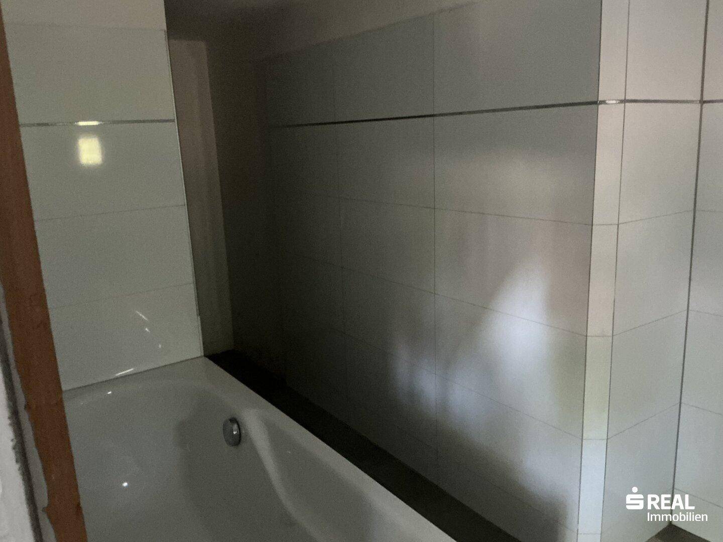 Badezimmer mit weiß gefliester Badewanne und hellen Wandfliesen, funktional und sauber.