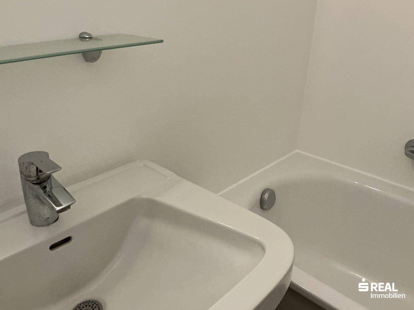 Helles Badezimmer mit Einzelwaschbecken, Badewanne und praktischer Glasablage.