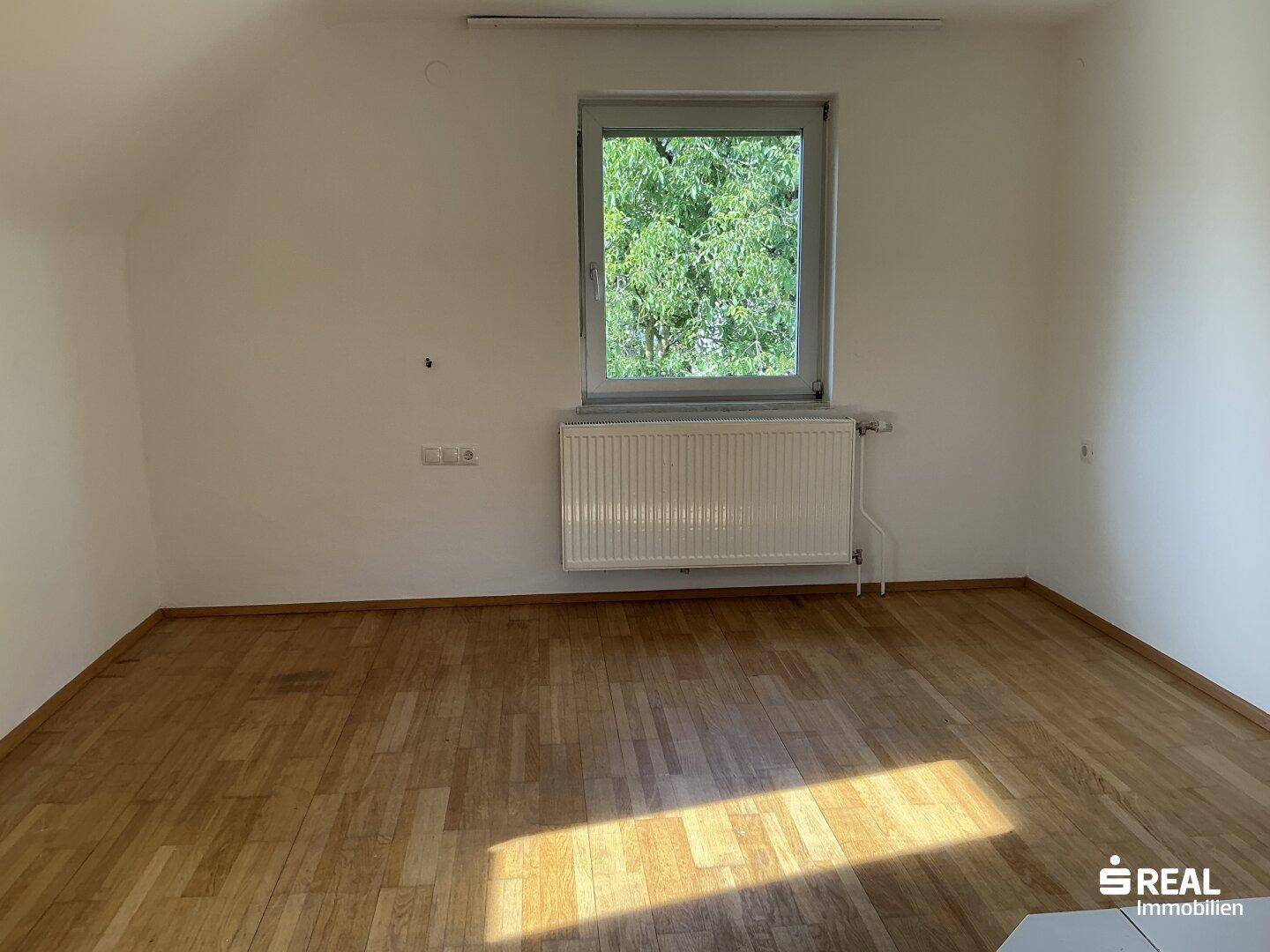 Helles Zimmer mit Holzdielenboden und einem Fenster mit Blick ins Grüne.
