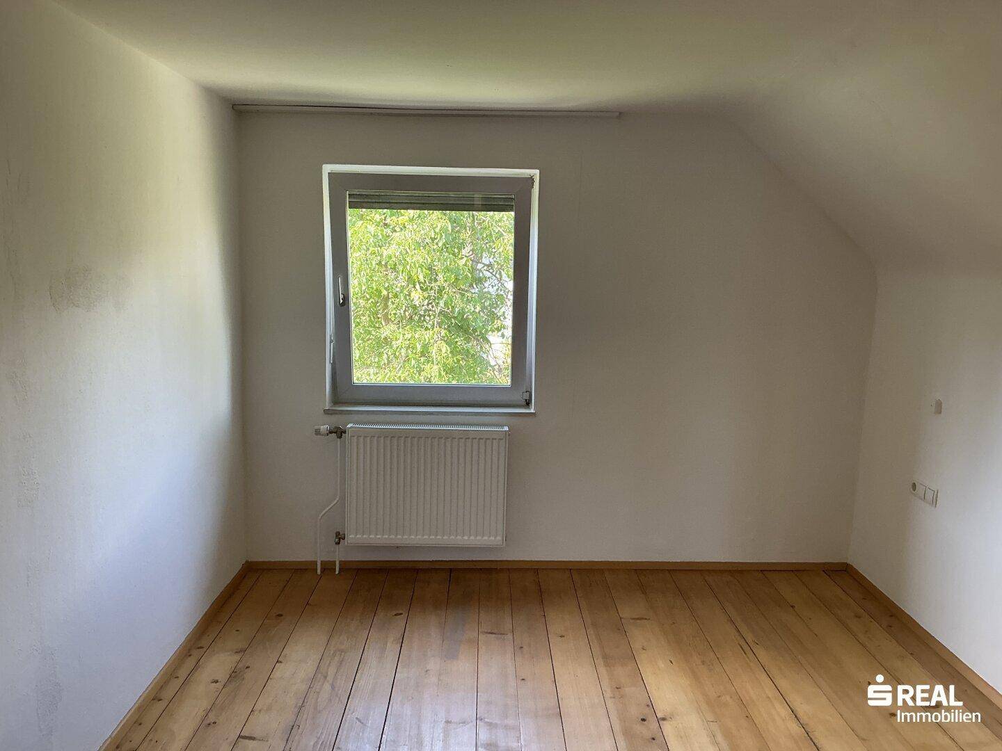 Helles Dachzimmer mit Holzdielenboden und Fenster, ideal als Schlaf- oder Arbeitszimmer.
