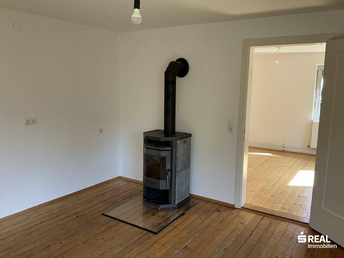 Gemütliches Zimmer mit Holzdielenboden und einem modernen Holzofen als Wärmequelle.