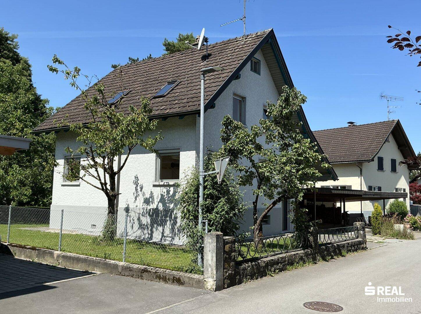 Seitenansicht des Hauses mit Satteldach, umzäuntem Vorgarten und Dachfenstern.