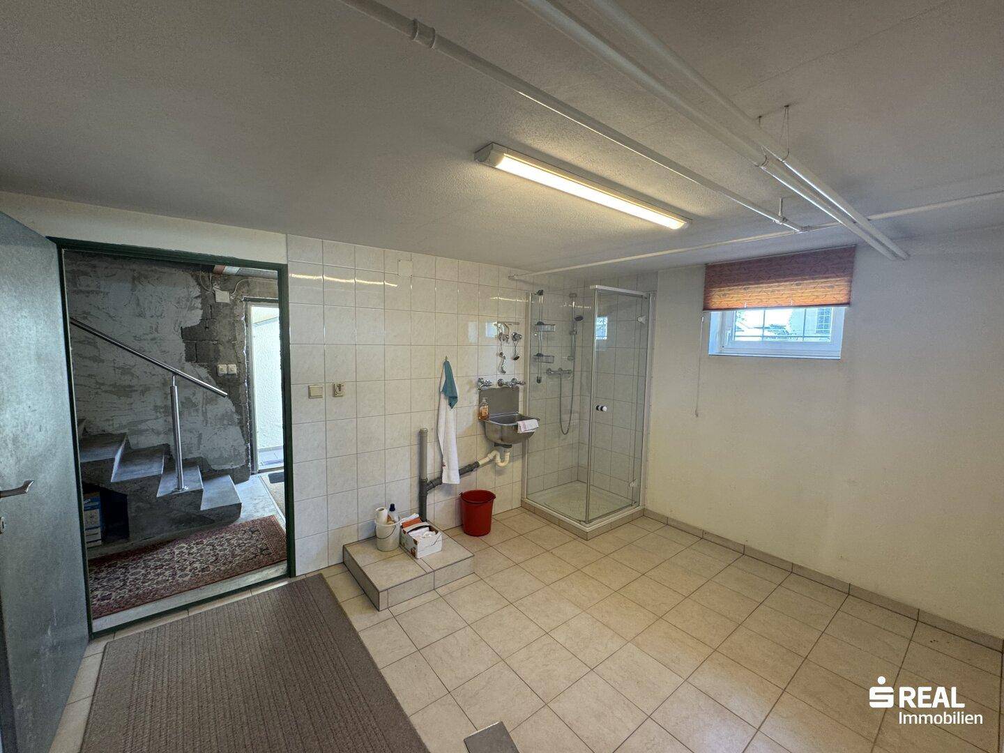 Gefliester Mehrzweckraum im Untergeschoss mit Dusche und Zugang zu einem weiteren Kellerbereich.