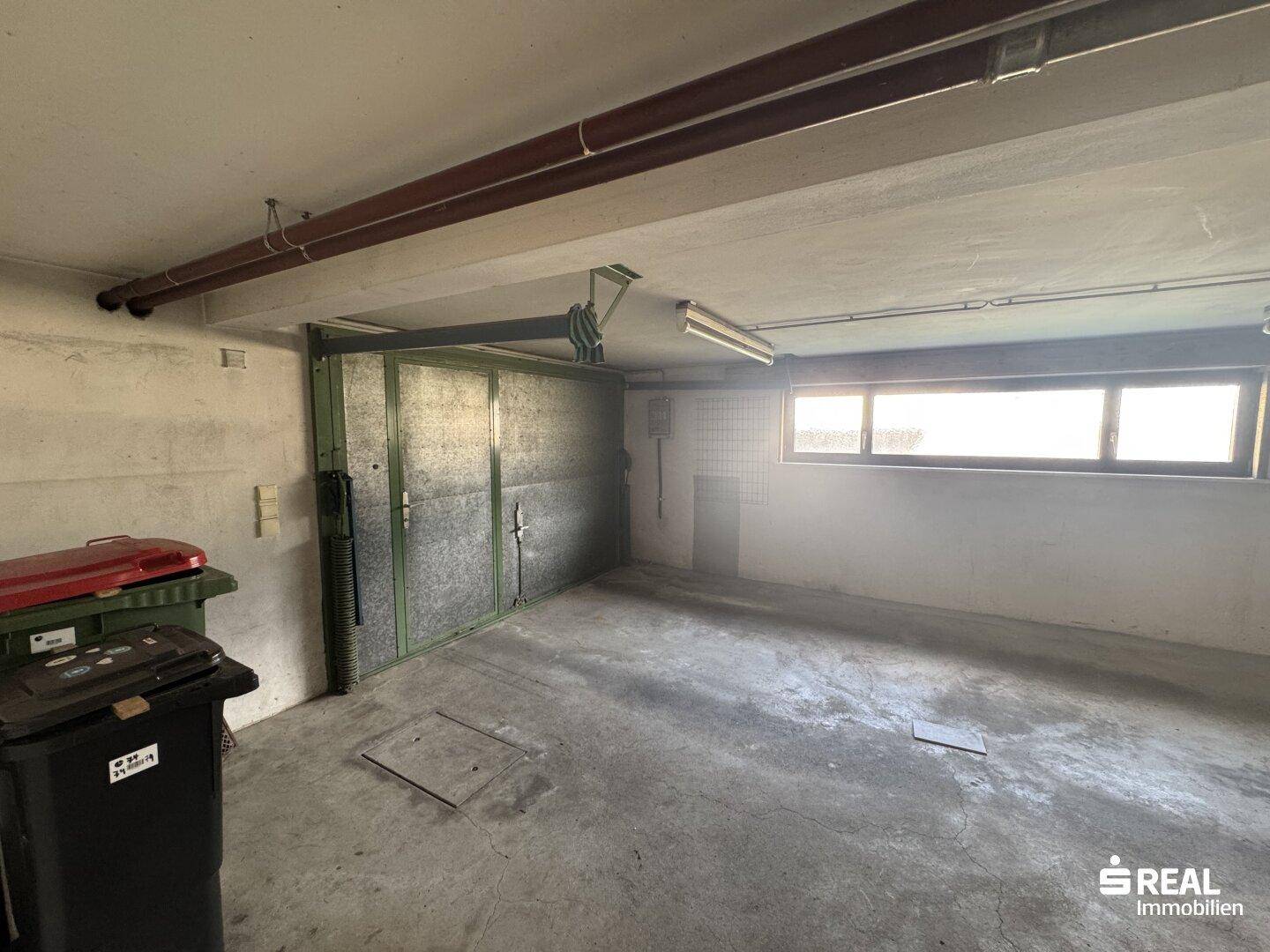 Geräumige Garage im Untergeschoss mit Rolltor und Fenster, bietet Platz für ein Fahrzeug.