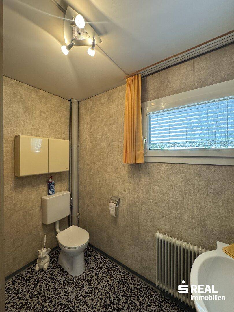 Kleines Gäste-WC mit Fenster, Heizkörper und gemusterten Tapeten im Retro-Stil.