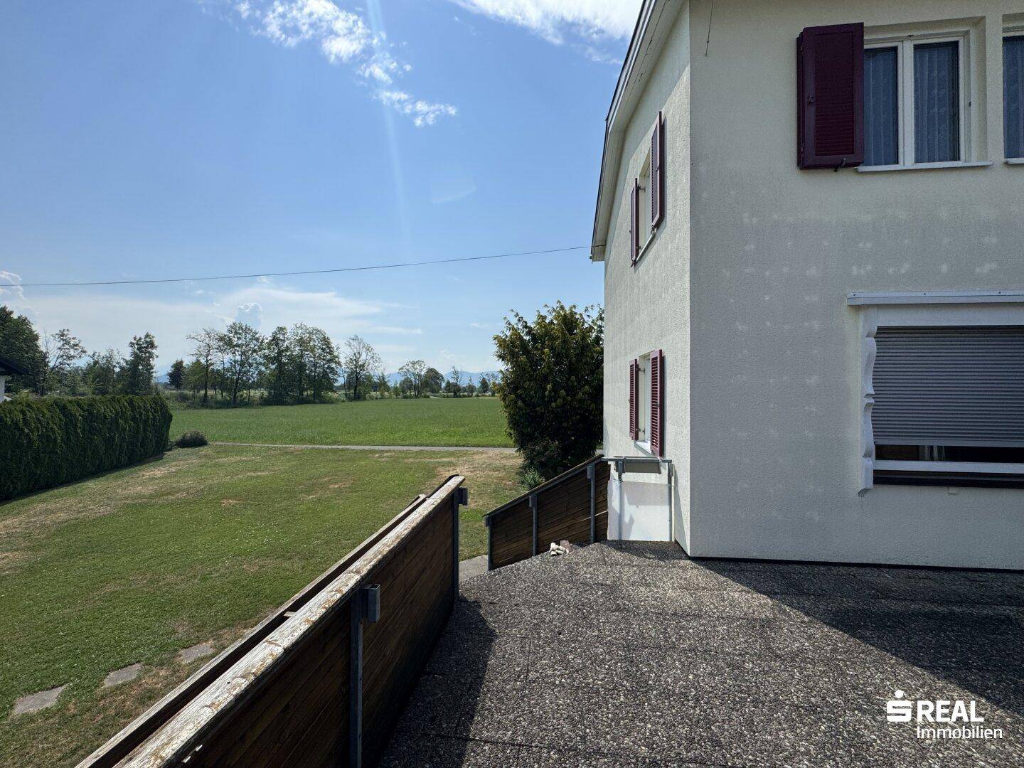 Seitenansicht des Hauses mit weitem Blick über grüne Felder und die ländliche Umgebung an einem sonnigen Tag.