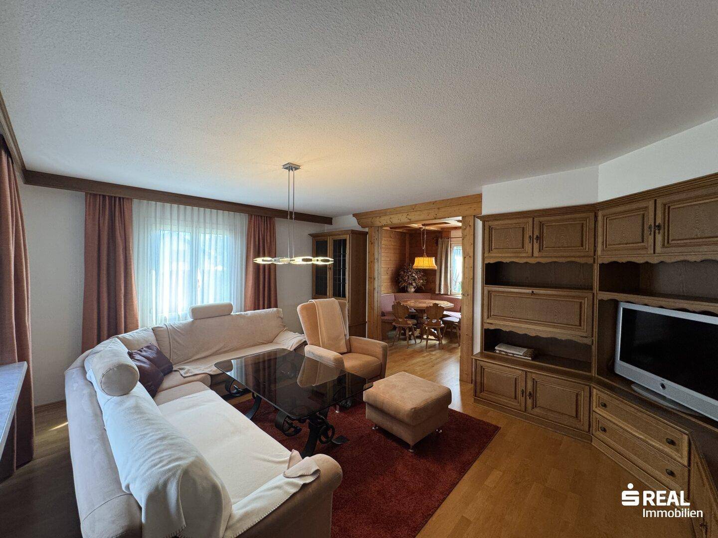 Geräumiges Wohnzimmer mit traditionellen Holzmöbeln, bequemer Couch und Blick in den Essbereich.