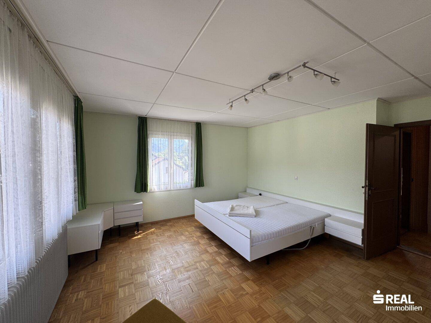 Helles Schlafzimmer mit Parkettboden, Doppelbett und Blick ins Grüne durch das Fenster.