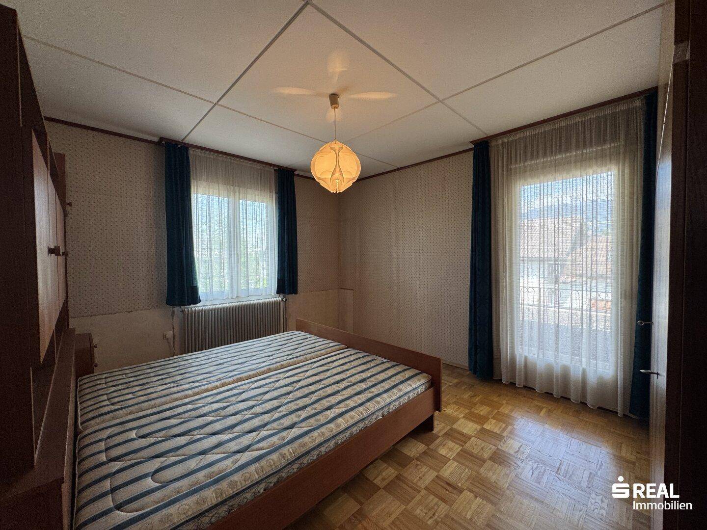 Geräumiges Schlafzimmer mit Parkettboden, Doppelbett und zwei Fenstern für viel Tageslicht.