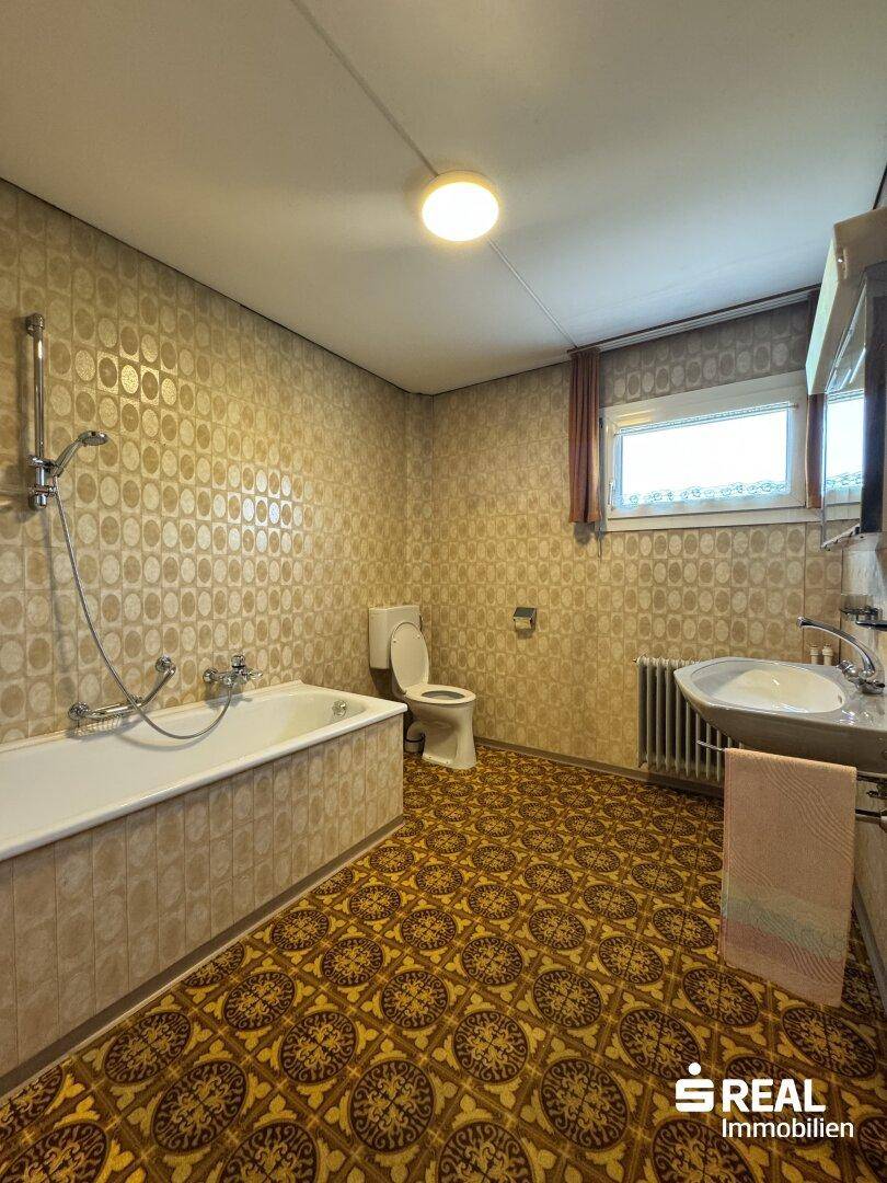 Badezimmer im Retro-Stil mit Badewanne, WC, Waschbecken und gemusterten Fliesen.
