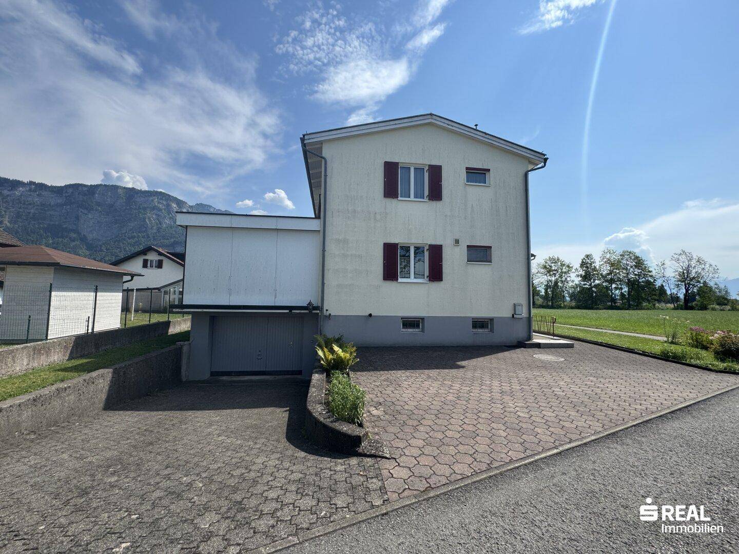 Seitenansicht des Hauses mit gepflasterter Auffahrt und Blick auf die umliegende Berglandschaft.