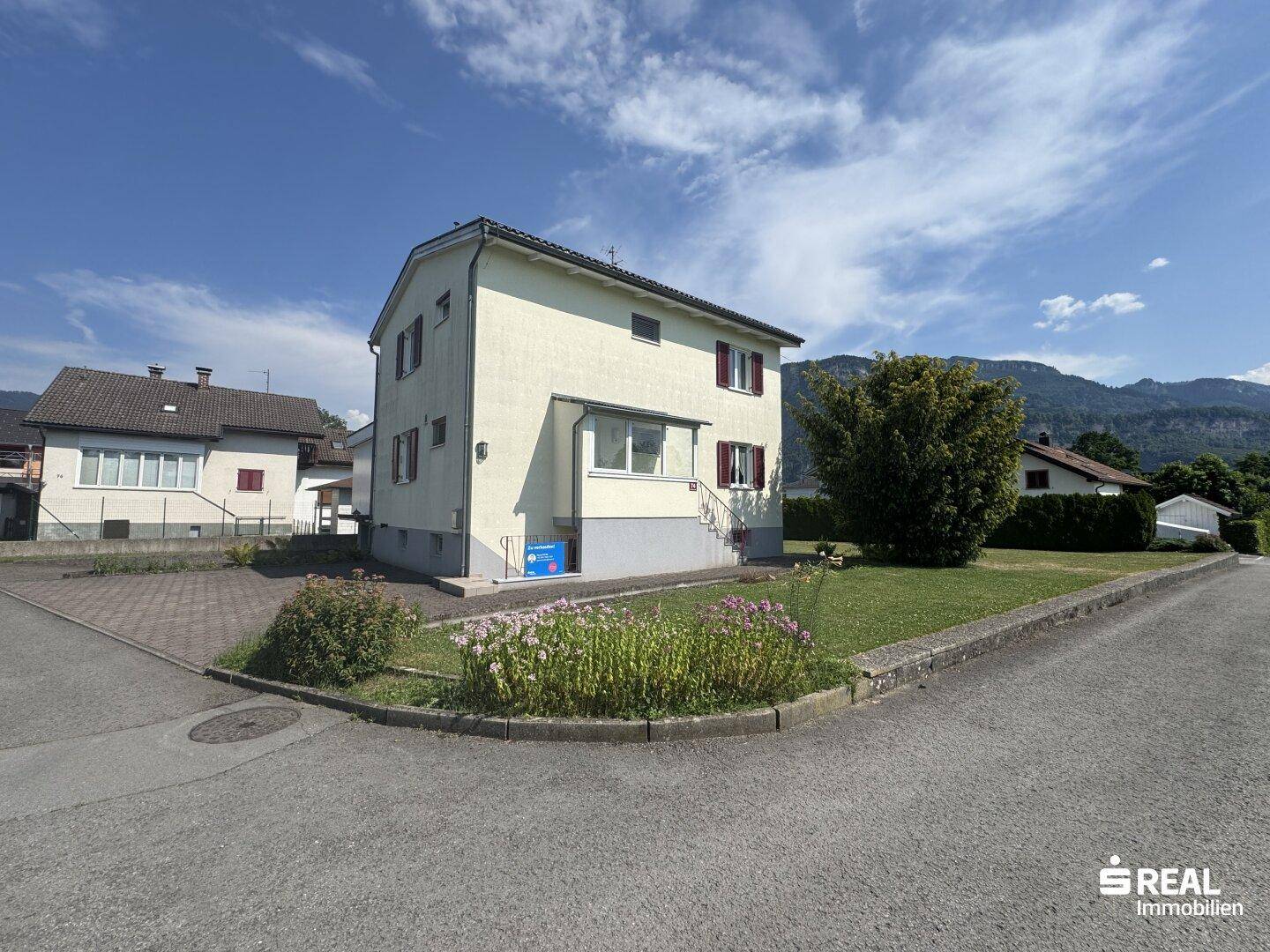 Vorderansicht des Hauses mit gepflegtem Vorgarten und Blumenbeeten an einer ruhigen Straße.