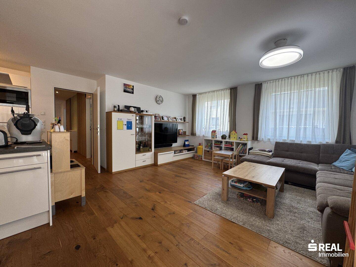 Offener Wohn- und Essbereich mit Holzboden, Sofa und Blick auf die moderne Küche.