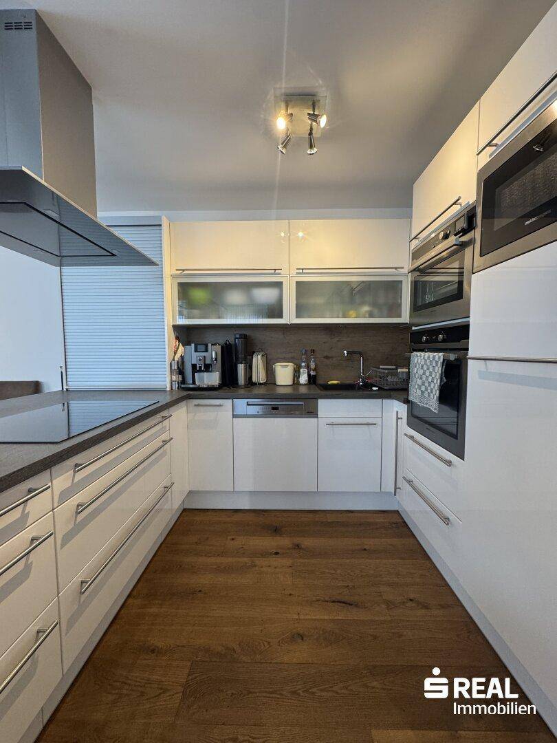 Moderne Küche mit weißen Hochglanzfronten, Induktionskochfeld und integrierten Geräten.