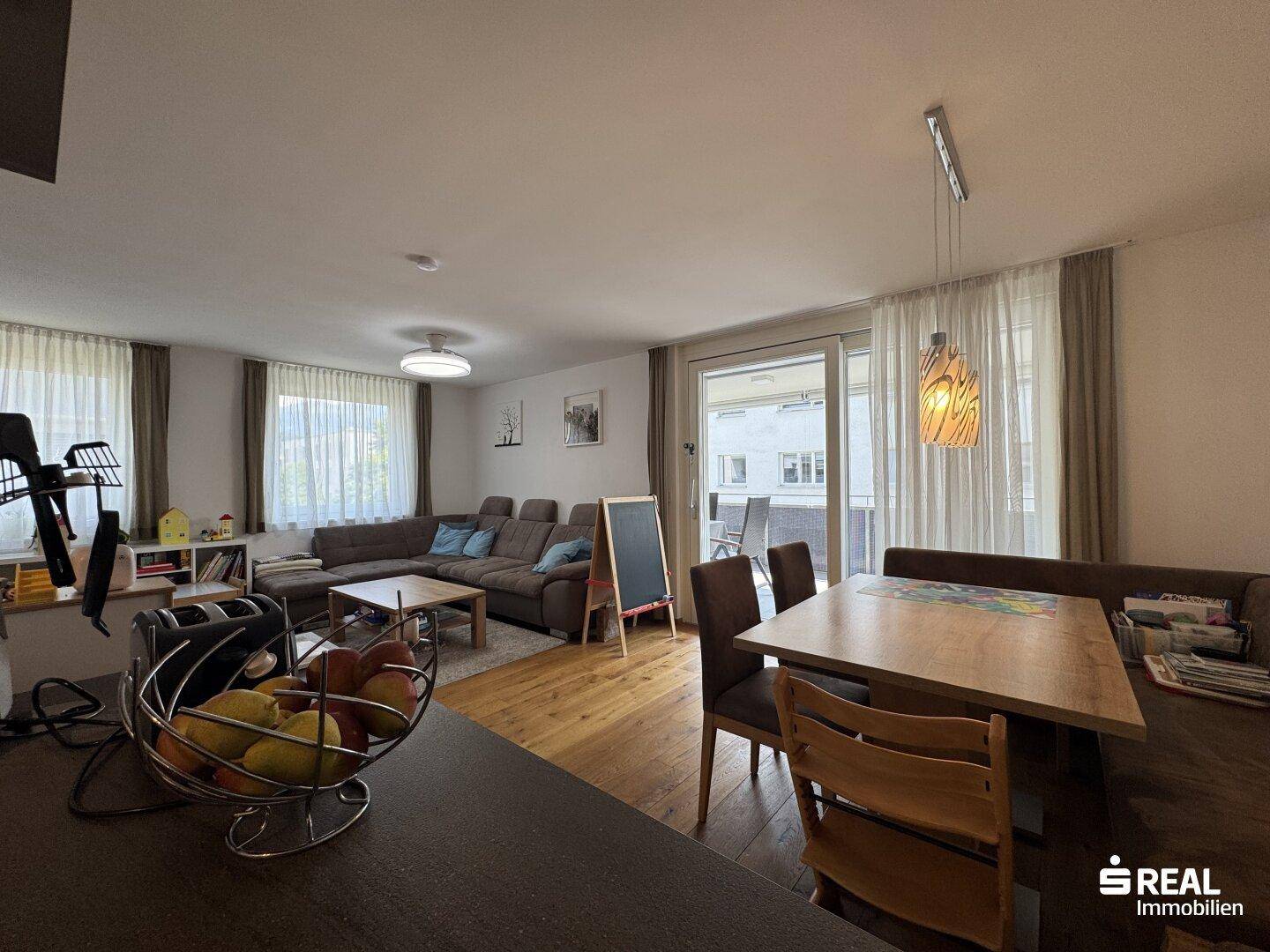 Geräumiger Wohn-Essbereich mit Holzboden, großem Esstisch und Zugang zum Balkon.