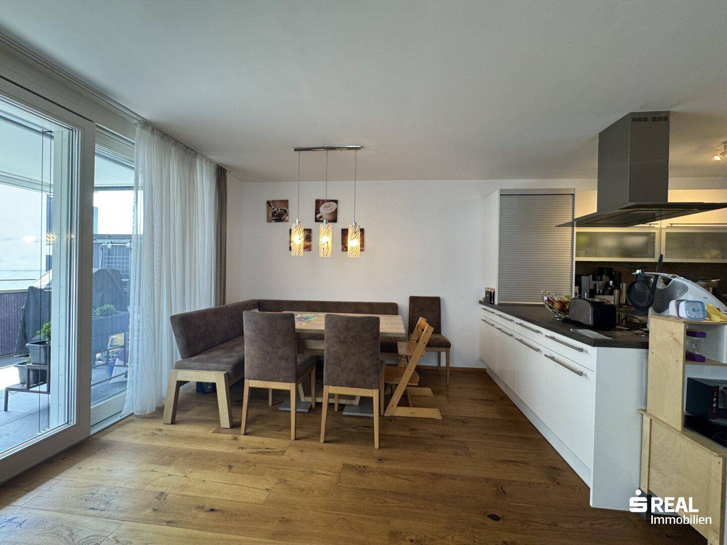 Heller Wohn-Essbereich mit offener Küche, Holzboden und direktem Zugang zum Balkon.