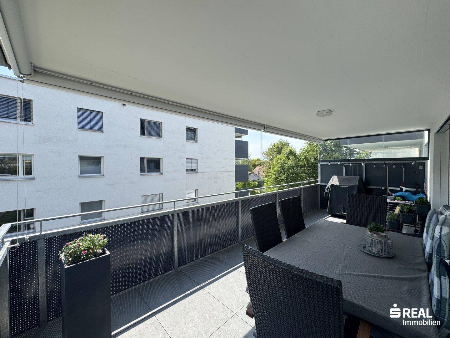 Großer Balkon mit Esstisch und Stühlen, ideal für Mahlzeiten im Freien mit Blick ins Grüne.