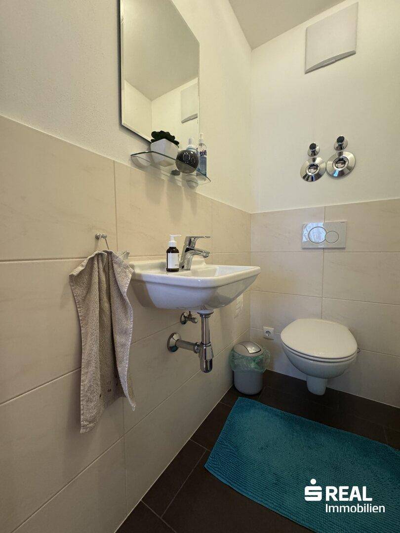 Kleines Gäste-WC mit modernem Waschbecken, Wand-WC und hellen Fliesen.