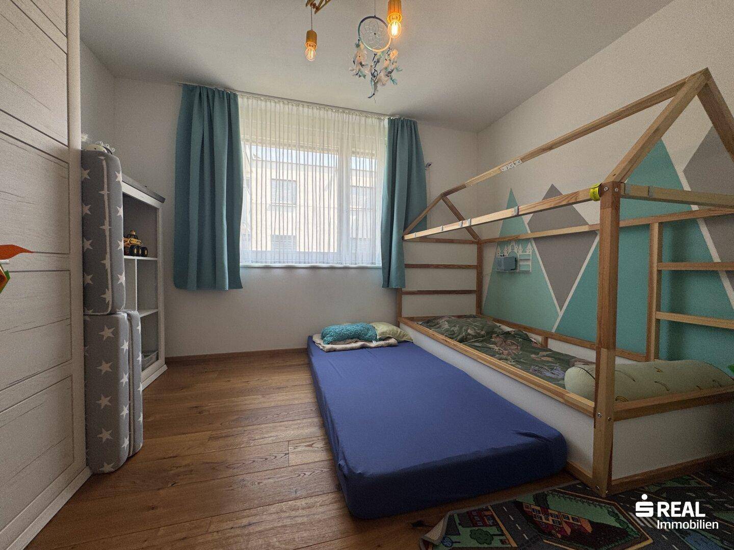 Kinderzimmer mit Holzboden, speziellem Bettgestell und viel Tageslicht durch das Fenster.