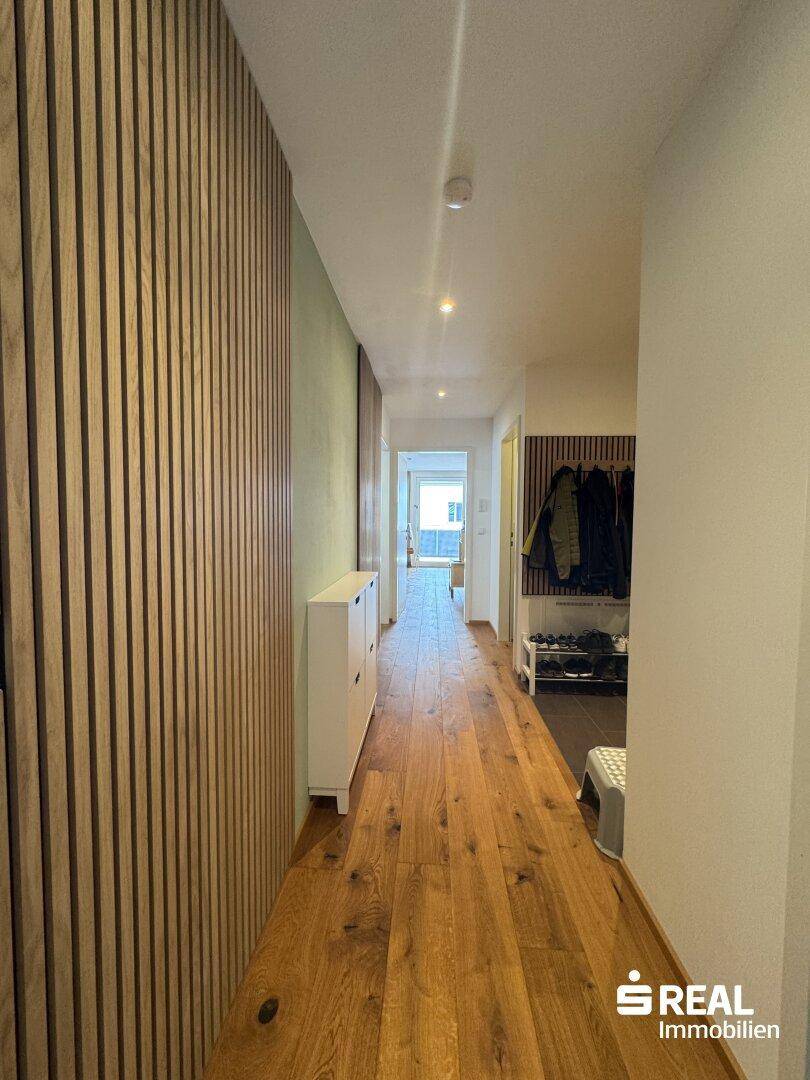 Heller Flur mit Holzboden und moderner Holzlamellenwand, die einen warmen Empfang bietet.