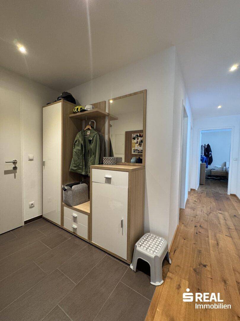 Eingangsbereich mit Garderobe, Spiegel und Fliesenboden, der in den Wohnbereich führt.