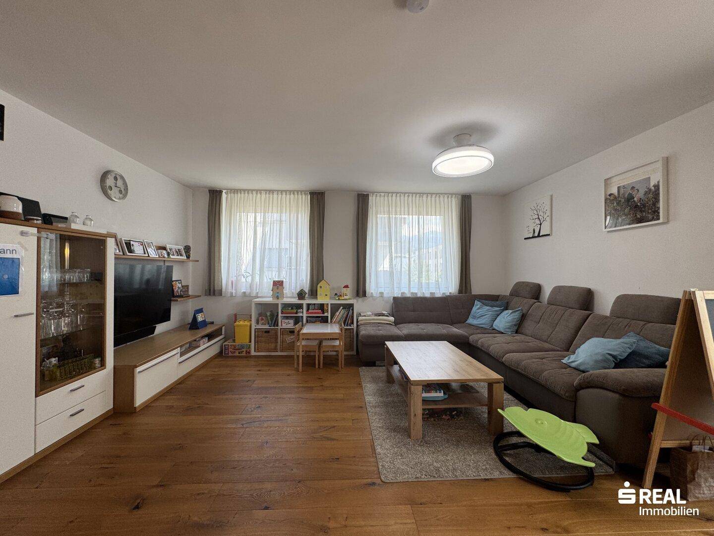 Geräumiges Wohnzimmer mit Holzboden, großem Sofa und Unterhaltungsmöbeln, hell und einladend.