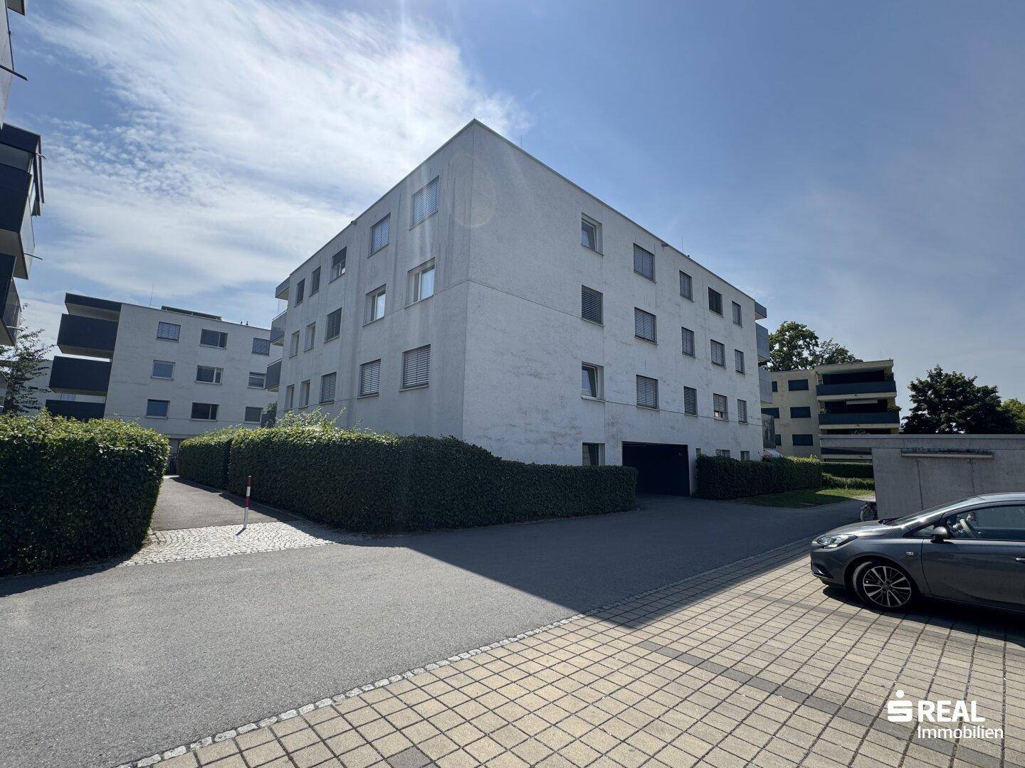 Moderne Wohnanlage mit weißer Fassade und gepflegten Hecken im Außenbereich.