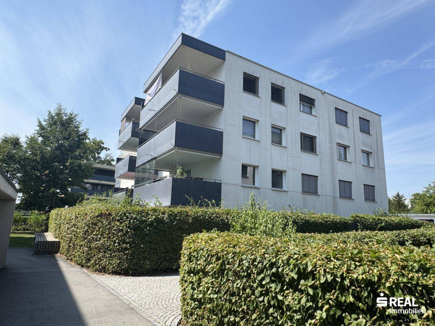 Ansicht der modernen Wohnanlage mit Balkonen und grüner Umgebung unter blauem Himmel.