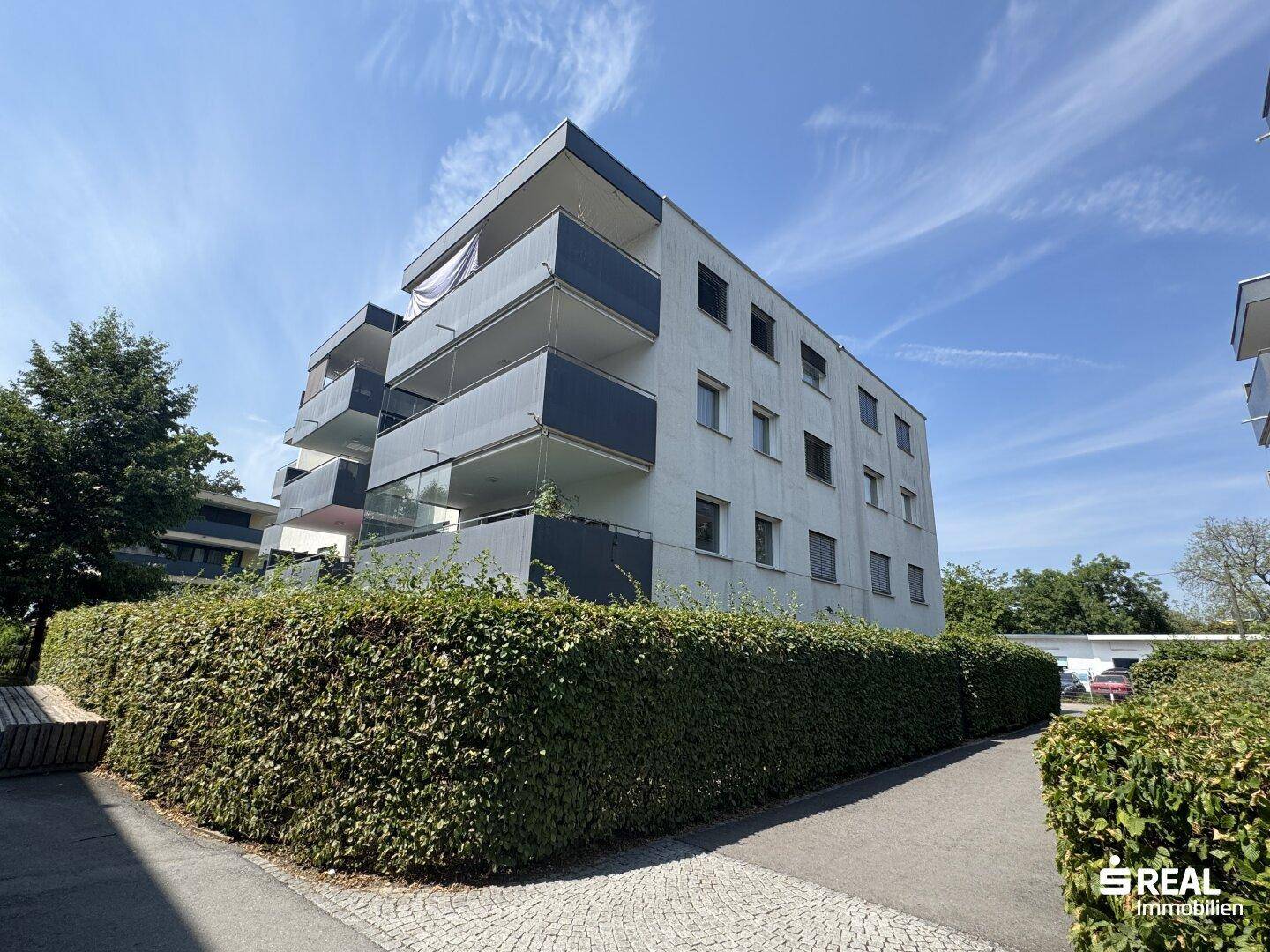 Außenansicht des Mehrfamilienhauses mit Balkonen und gepflegter Hecke, umgeben von Natur.
