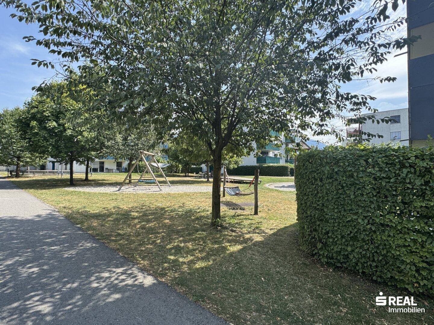 Grüner Außenbereich mit Kinderspielplatz, Schaukeln und viel Rasenfläche für Familien.