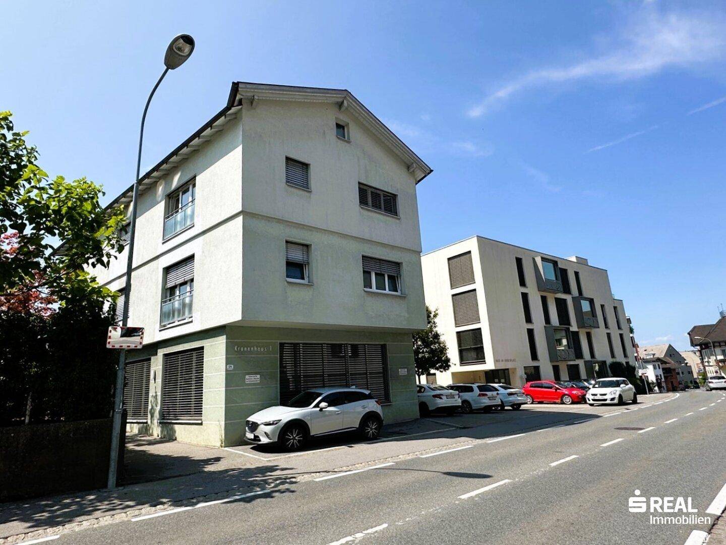 Ansicht des modernen Gebäudes von der Straße aus, mit weiteren Gebäuden und geparkten Autos.