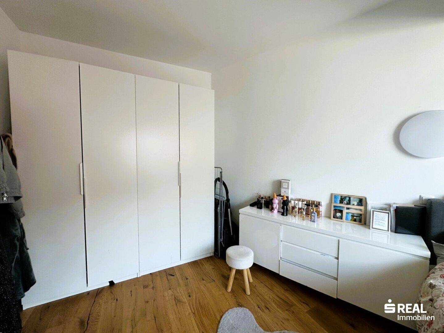 Schlafzimmer mit großem weißen Kleiderschrank, Kommode und Holzboden.
