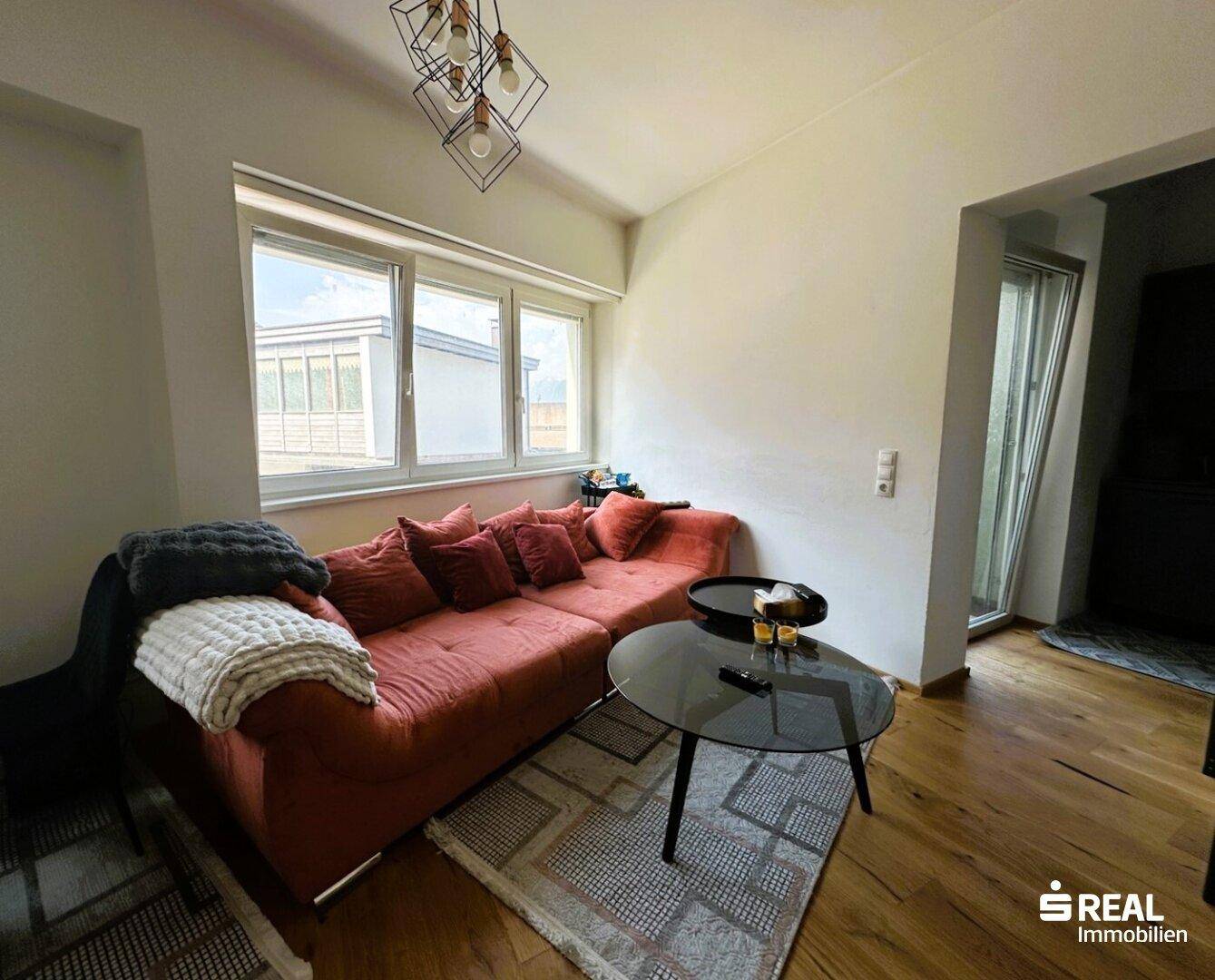 Gemütliches Wohnzimmer mit einem großen orangefarbenen Sofa, Couchtisch und Holzboden.