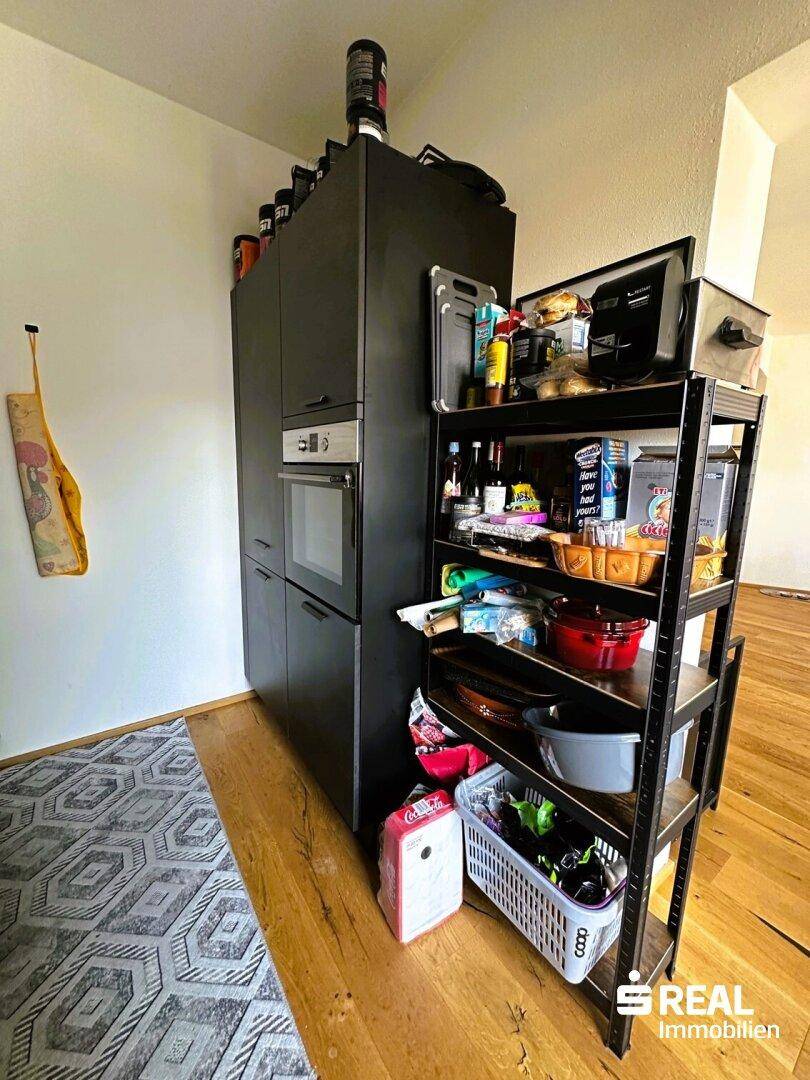 Küchenbereich mit hohem Schrank, integriertem Backofen und offenem Regal für Vorräte.