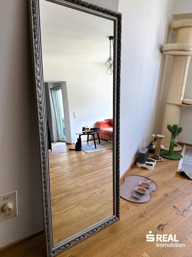 Großer Standspiegel im Wohnbereich, der den Raum mit Holzboden und Sofa widerspiegelt.