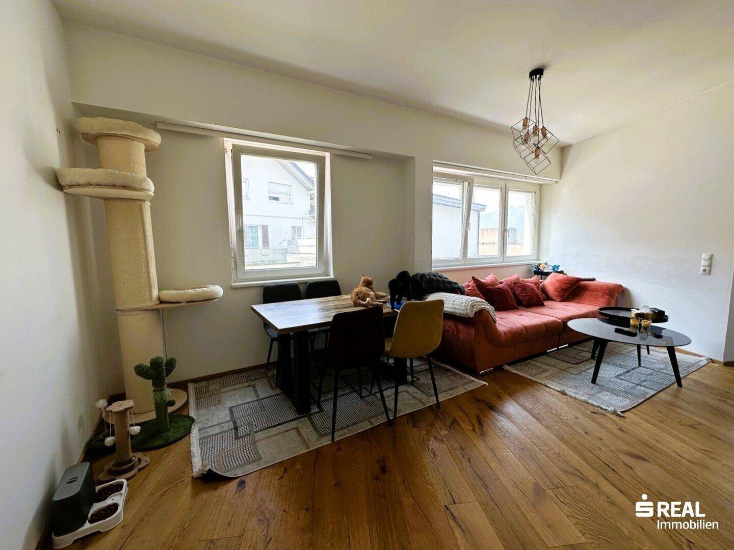 Gemütlicher Wohn-Essbereich mit Holzboden, Esstisch, Sofa und einem Katzenkratzbaum.
