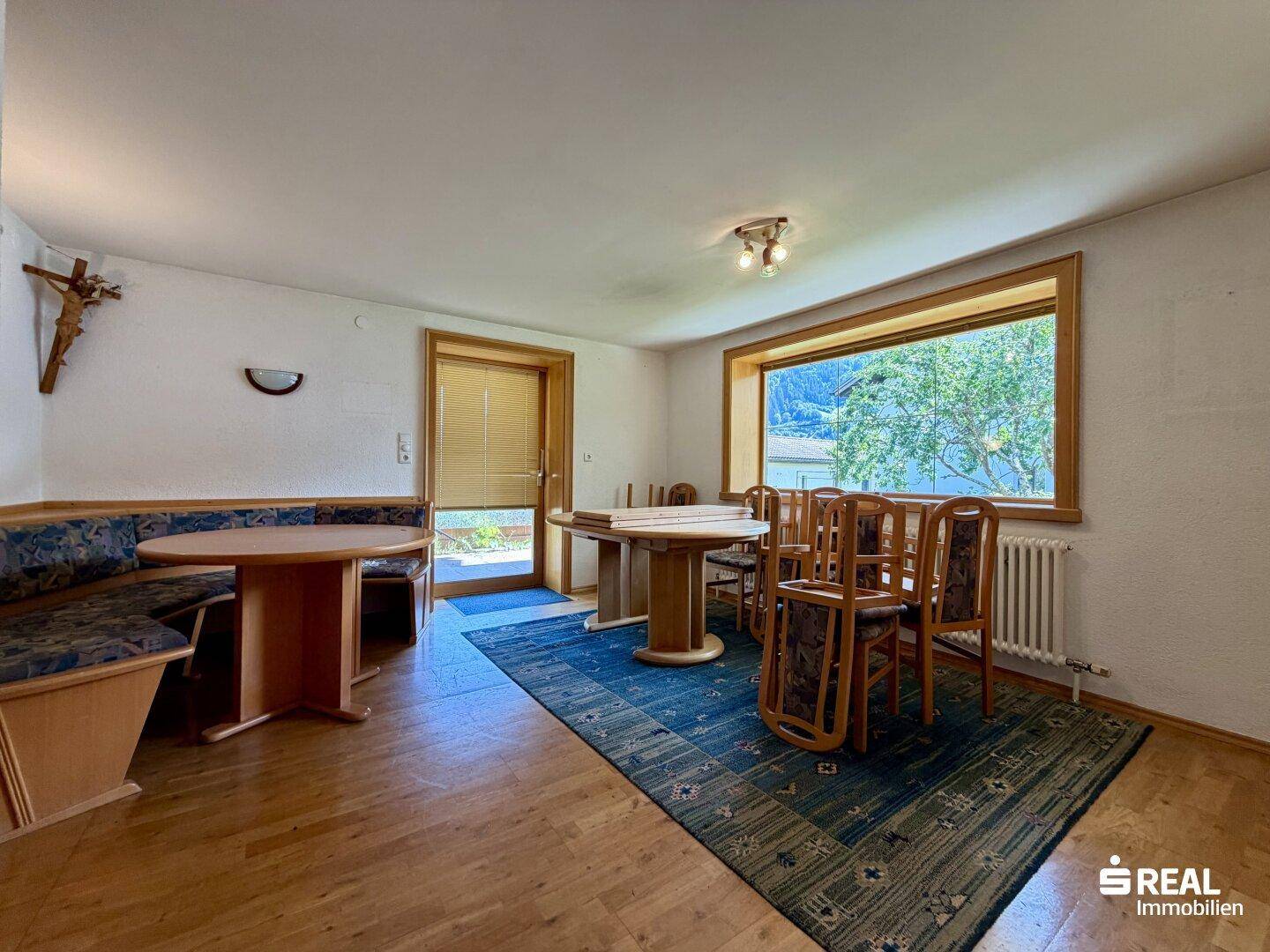 Gemütlicher Essbereich mit Holzbänken, großem Fenster und Blick auf die umliegende Natur.