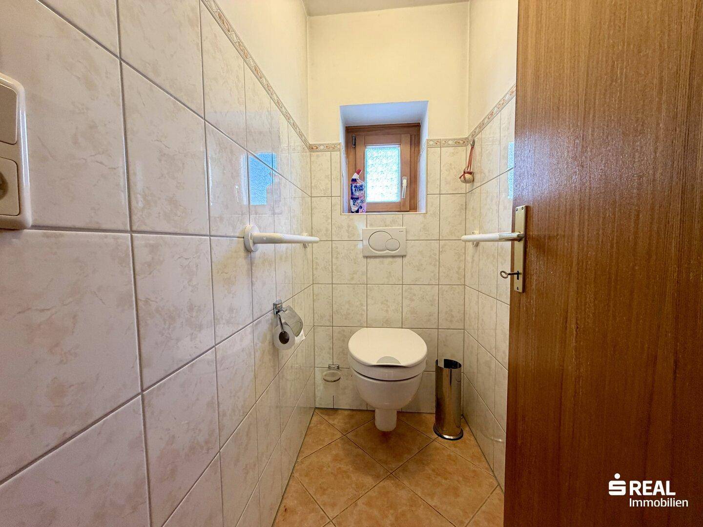 Separates WC mit hellen Fliesen und einem kleinen Fenster für Tageslicht.